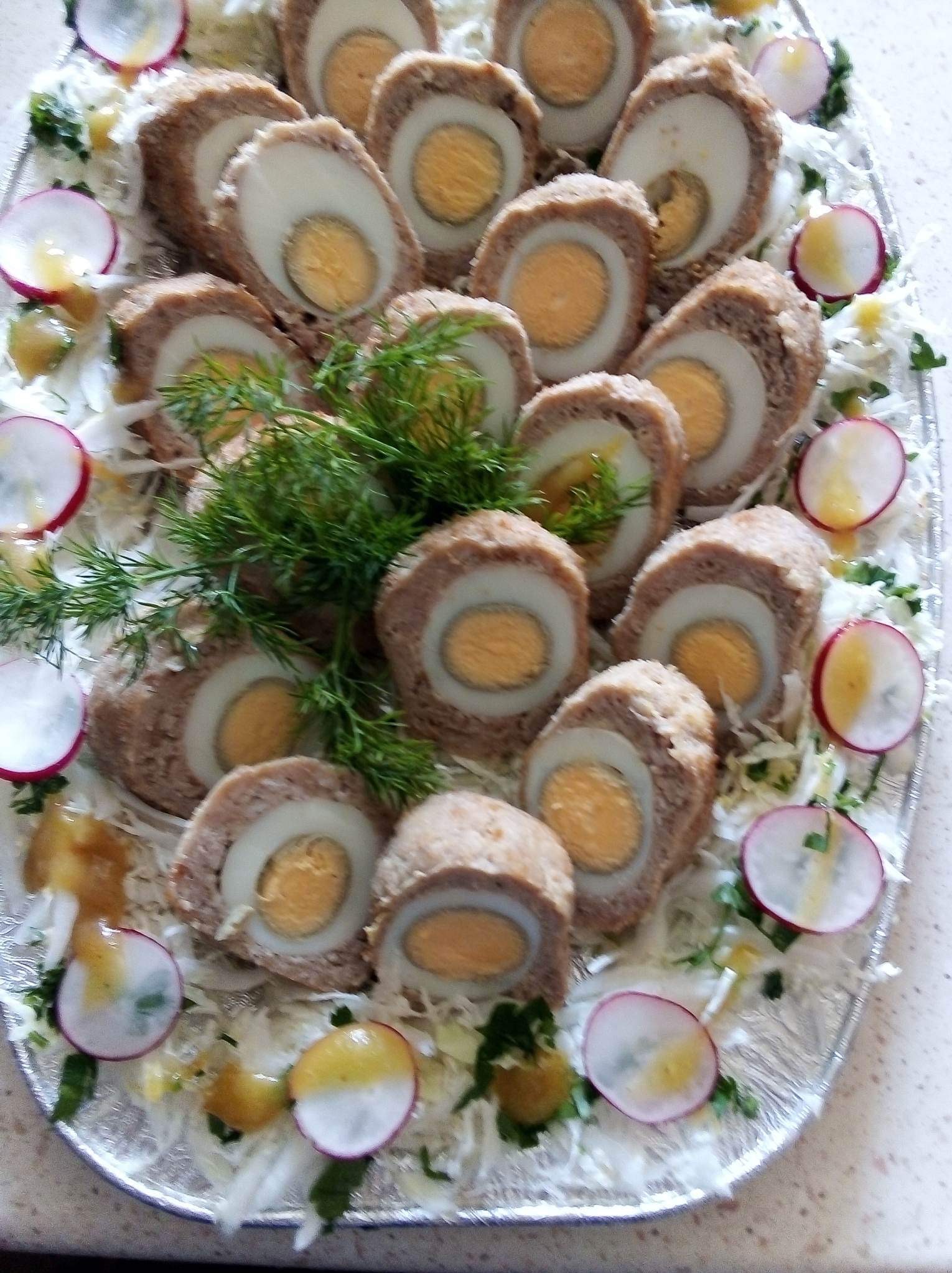 Dekoracyjna taca z jajkami w otoczce mięsnej, przyozdobiona rzodkiewką, kapustą i koperkiem. Idealna przekąska na przyjęcie lub uroczystość.