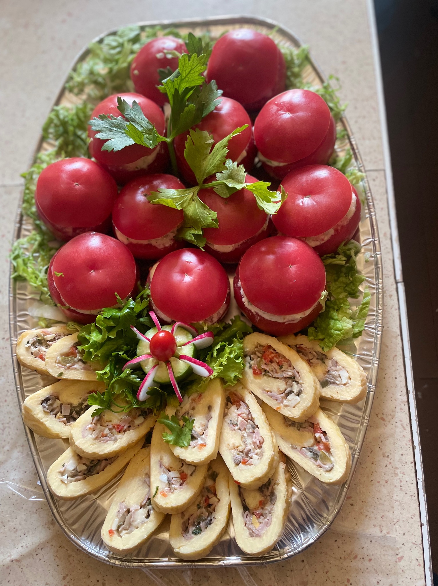 Elegancka kompozycja: pomidory faszerowane i roladki z farszem na srebrnej tacy, udekorowane sałatą i rzodkiewką. Idealne na przyjęcie.