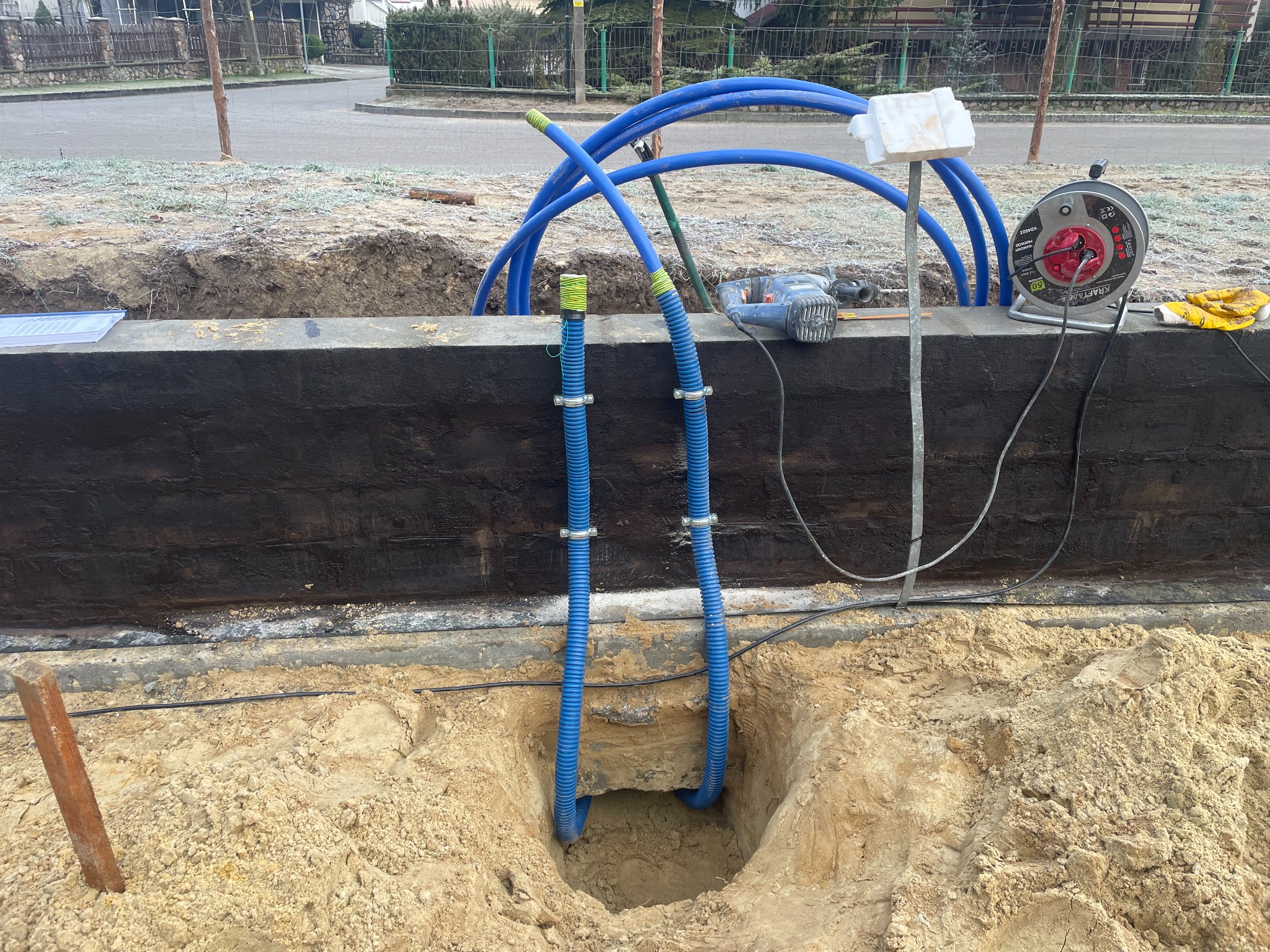 Instalacja rur w wykopie pod fundament domu w Grudziądzu. Widoczne narzędzia i przewody. Etap budowy domu.