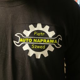 MARTYNA SZWED - Czarna koszulka z nadrukiem logo warsztatu samochodowego, widoczny tatuaż na szyi modela. Żółto-biały nadruk z nazwą 'Auto Naprawa Piotr Szwed'.