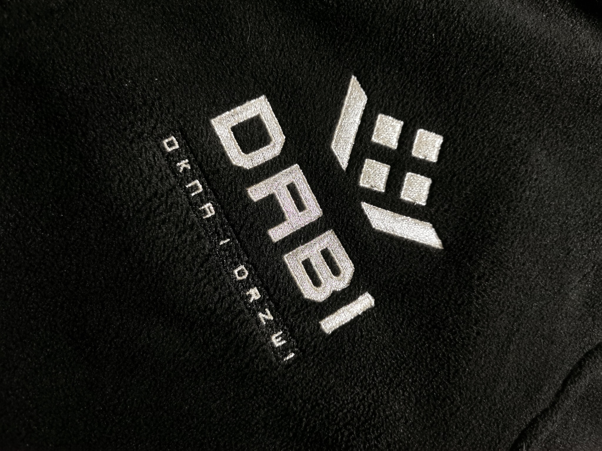 Czarna bluza z haftowanym, srebrnym logo 'DRABI OKNA I DRZWI'. Widoczna faktura materiału i precyzyjne wykonanie haftu.