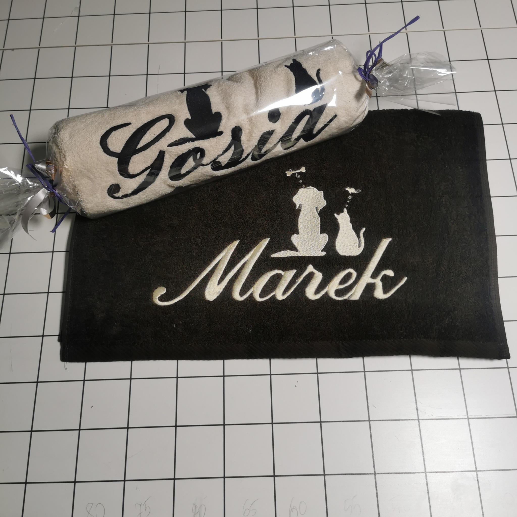 Haftowane ręczniki z imionami 'Gosia' i 'Marek' oraz motywami zwierzęcymi (kot i pies) na białym, kwadratowym tle.