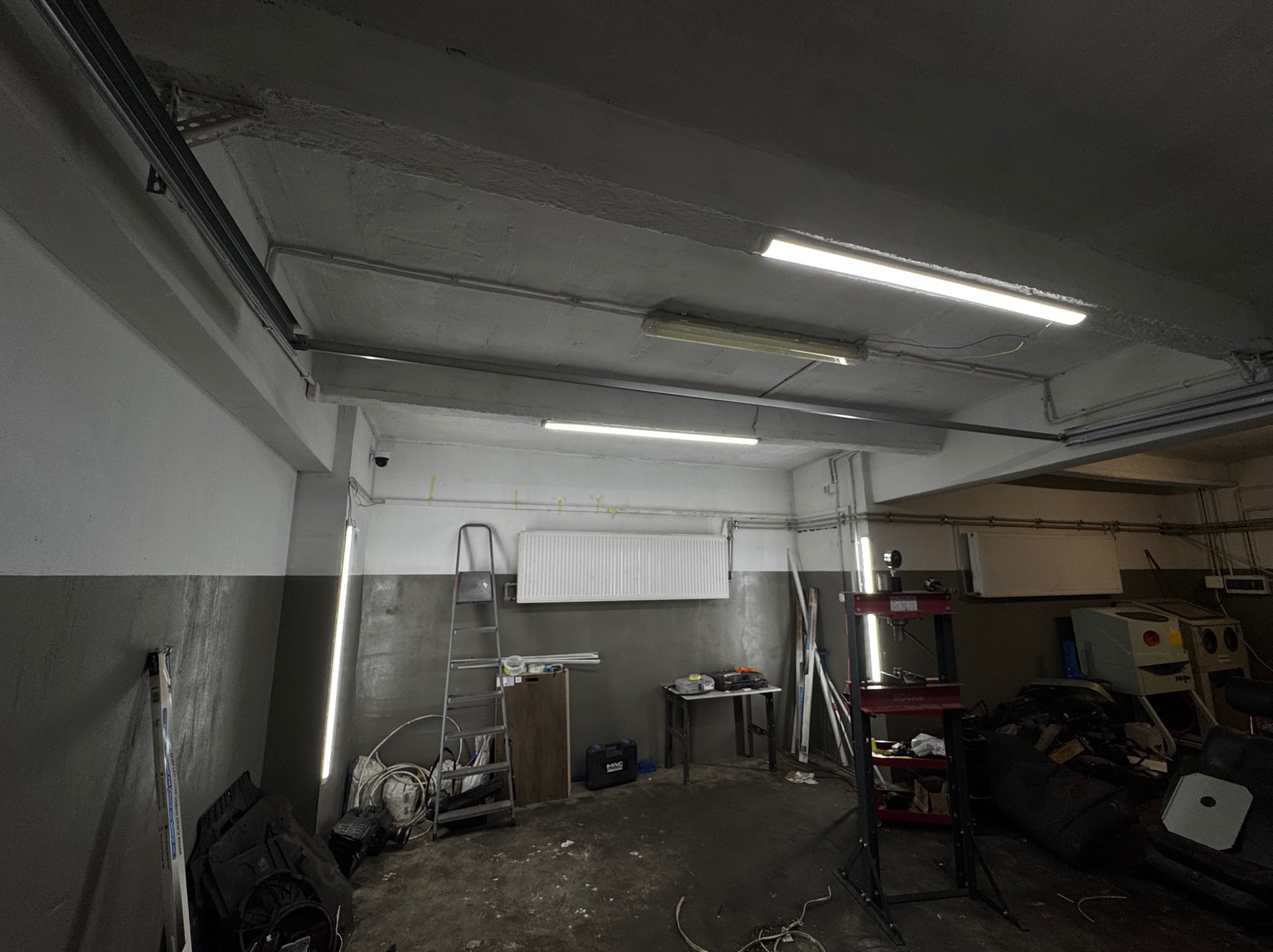 Wnętrze warsztatu w Rzeszowie z zamontowanym oświetleniem LED na suficie. Widoczne przewody i elementy instalacji. Biało-szare ściany, drabina i narzędzia.