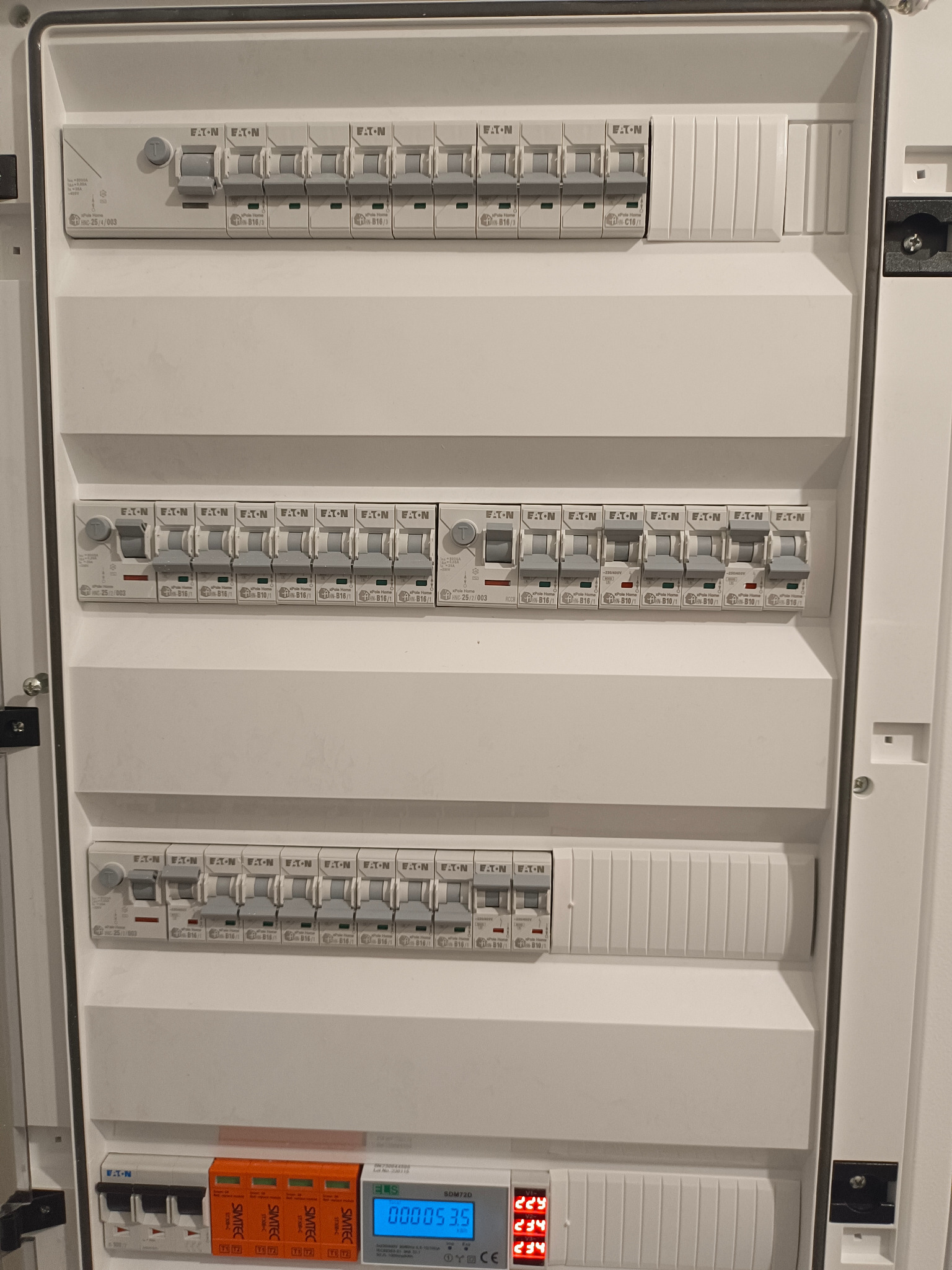 Rozdzielnica elektryczna Eaton z zabezpieczeniami, modułami SMITEC i wyświetlaczem EMS SDM720, ukazująca stan instalacji. Widok z bliska na białą obudowę i komponenty.