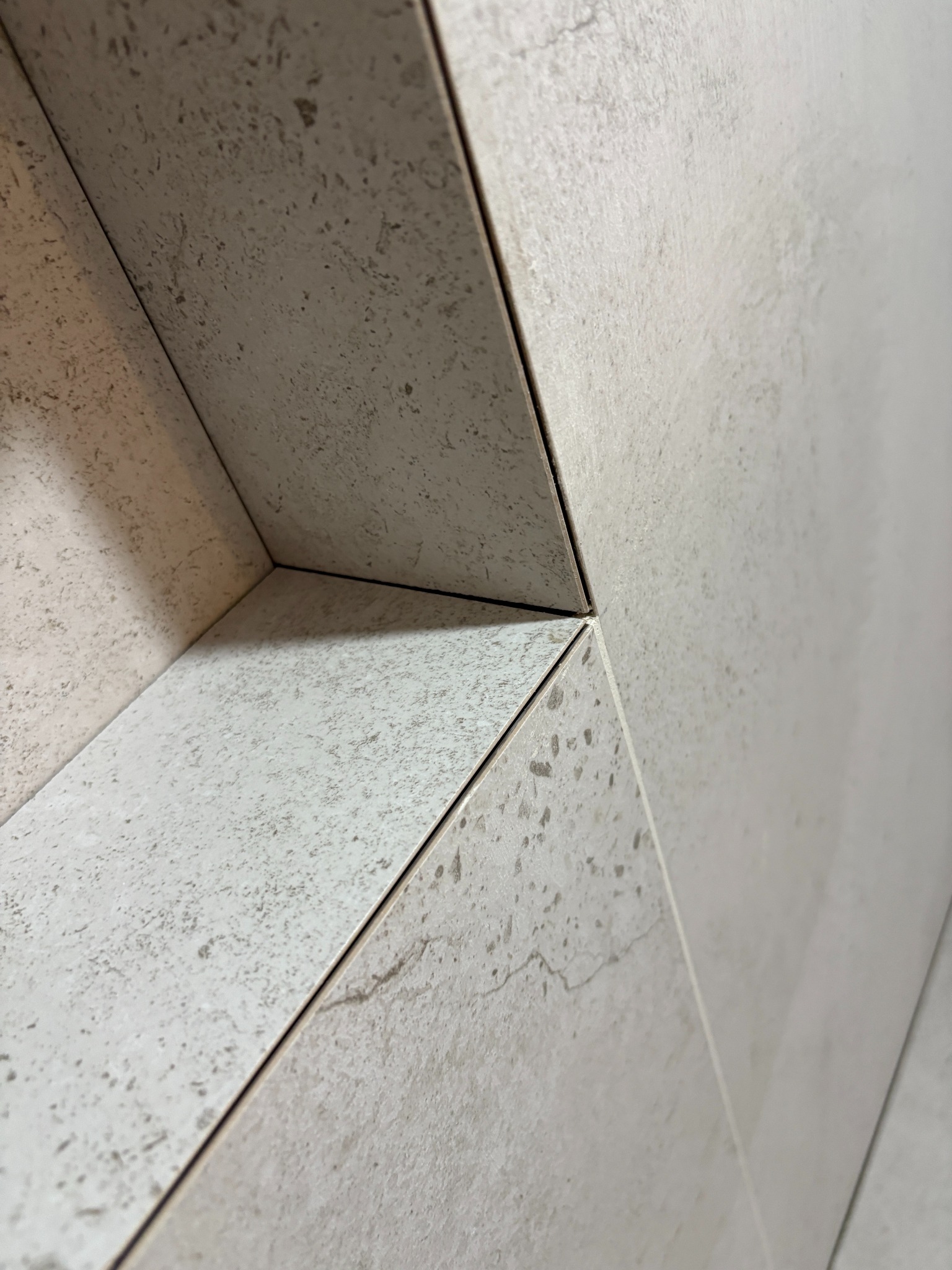 Szczegółowe ujęcie narożnika wykończonego jasnymi, beżowymi płytkami imitującymi kamień, z precyzyjnie wykonanymi fugami, ukazujące dokładność i estetykę wykończenia.