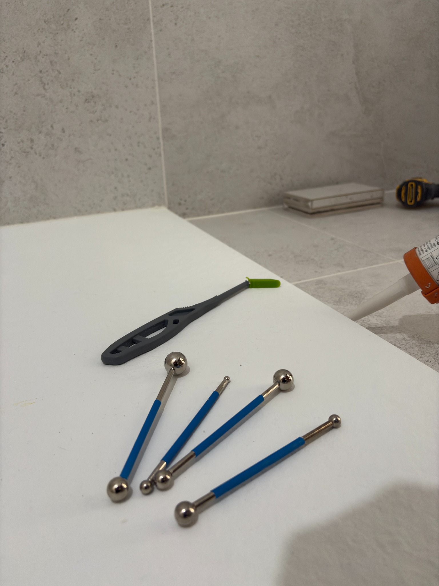 Narzędzia do fugowania na tle płytek i białej powierzchni. Widoczny aplikator silikonu. Detal z bliska, prezentujący precyzję prac wykończeniowych w łazience.