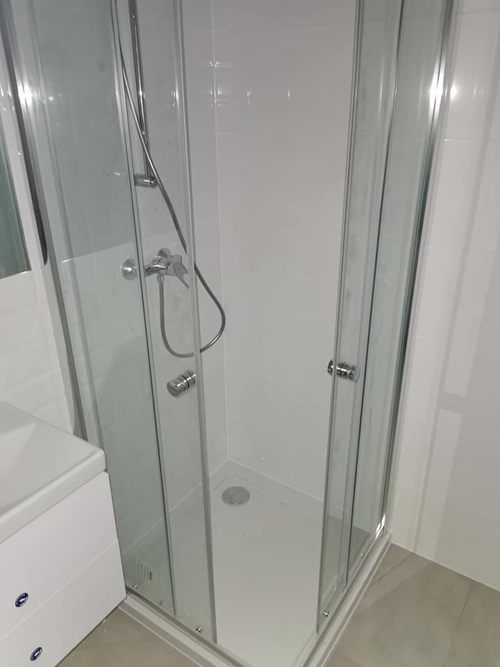 Nowoczesna kabina prysznicowa z chromowanymi detalami i białymi płytkami w tle. Minimalistyczny design, czyste linie i jasne wnętrze.