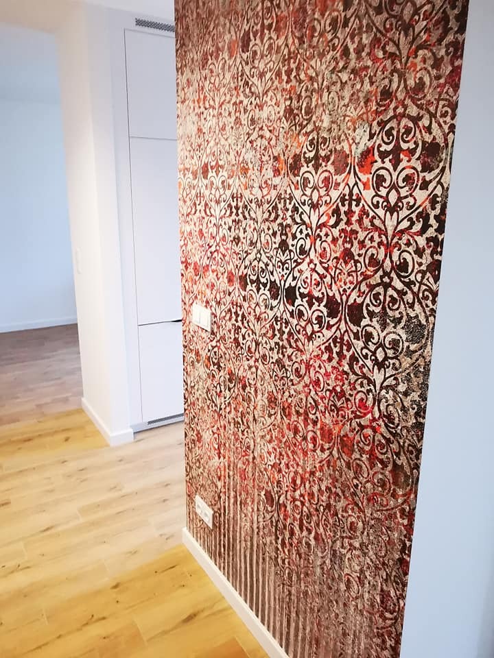 Wnętrze po wykończeniu: wzorzysta tapeta w odcieniach czerwieni i brązu na ścianie, jasna podłoga imitująca drewno, białe listwy przypodłogowe i fragment szafy wnękowej.