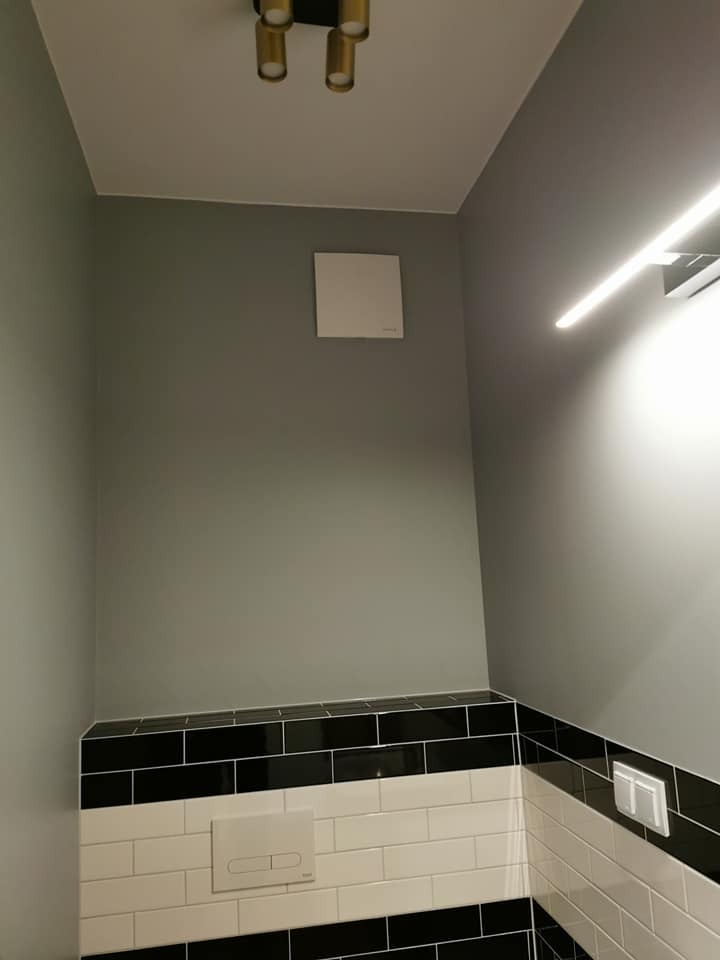 Szaro-biała łazienka z czarnymi akcentami: płytki, oświetlenie LED, wentylator. Minimalistyczny design, nowoczesne wykończenie.