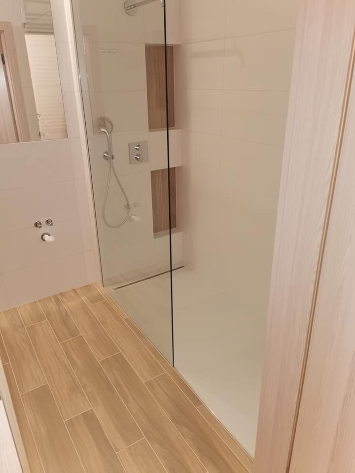 Nowoczesna kabina prysznicowa typu walk-in z drewnopodobną podłogą i wnękami w ścianie wykończonymi drewnem, tworząca minimalistyczny i elegancki design łazienki.