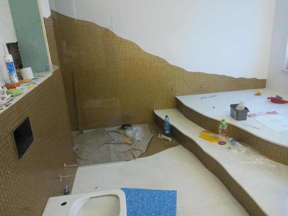 Mozaika w odcieniach złota, ułożona falą na ścianach i obudowie wanny w trakcie remontu łazienki. Widoczne narzędzia i materiały budowlane.