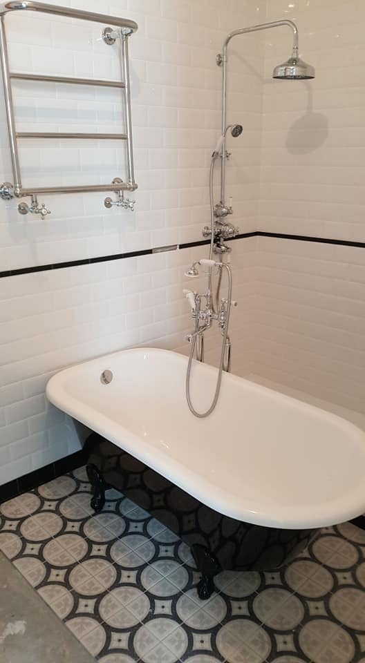 Elegancka łazienka z wolnostojącą wanną na lwich nóżkach, chromowaną armaturą i grzejnikiem drabinkowym. Białe płytki imitujące cegłę z czarnym akcentem.