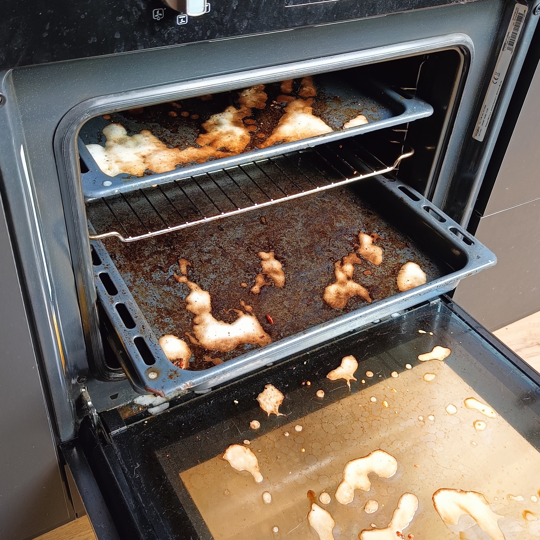 Brudny piekarnik z przypalonymi resztkami jedzenia na blachach i dnie, widoczne zabrudzenia i tłuszcz. Stan przed czyszczeniem.