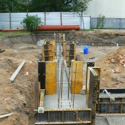 EX-BUD 78 SPÓŁKA Z OGRANICZONĄ ODPOWIEDZIALNOŚCIĄ - Zalewanie fundamentów zbrojonych w szalunkach. Widok na plac budowy w Warszawie. W tle widoczny płot z blachy falistej i fragment budynku.