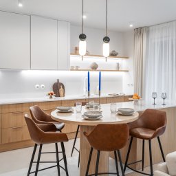 Miód Studio Weronika Babij - Nowoczesna aranżacja kuchni z okrągłym stołem i skórzanymi krzesłami barowymi w Gdyni. Jasne drewno, minimalistyczne lampy i dekoracje tworzą przytulną atmosferę.