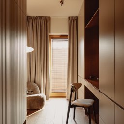 Miód Studio Weronika Babij - Neutralna kolorystyka gabinetu: drewniane panele ścienne, biurko z szafkami, krzesło i fotel boucle. Okno z żaluzjami i zasłonami w tle. Ciepłe, naturalne światło.