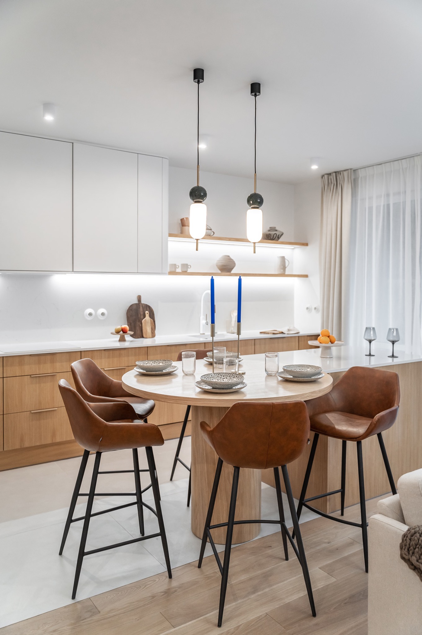 Nowoczesna aranżacja kuchni z okrągłym stołem i skórzanymi krzesłami barowymi w Gdyni. Jasne drewno, minimalistyczne lampy i dekoracje tworzą przytulną atmosferę.