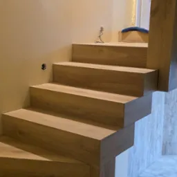 Wykończone schody z drewnopodobnych paneli, z widocznym otworem na gniazdko na ścianie i narzędziami w tle, ukazujące precyzję wykonania.