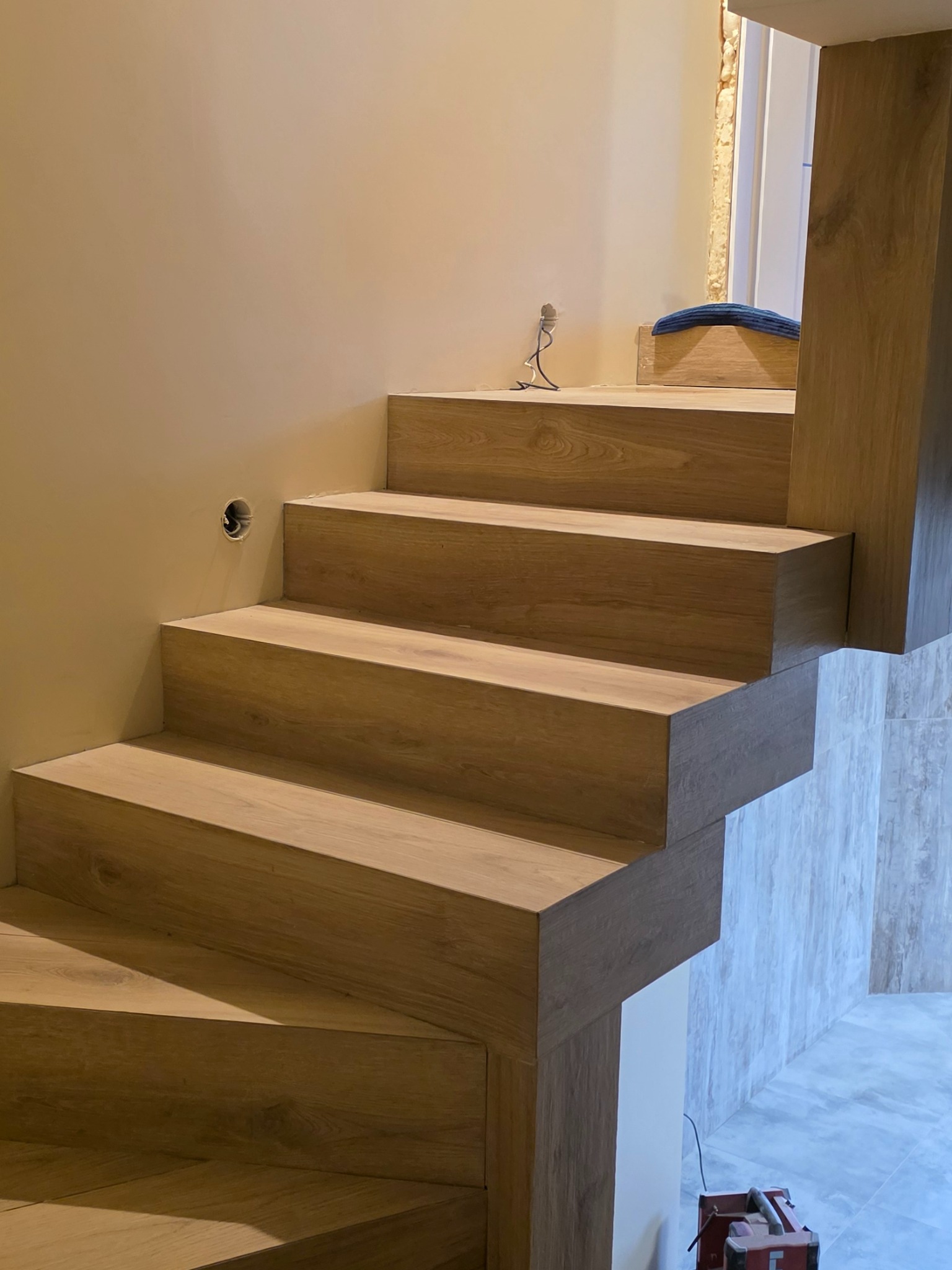 Wykończone schody z drewnopodobnych paneli, z widocznym otworem na gniazdko na ścianie i narzędziami w tle, ukazujące precyzję wykonania.