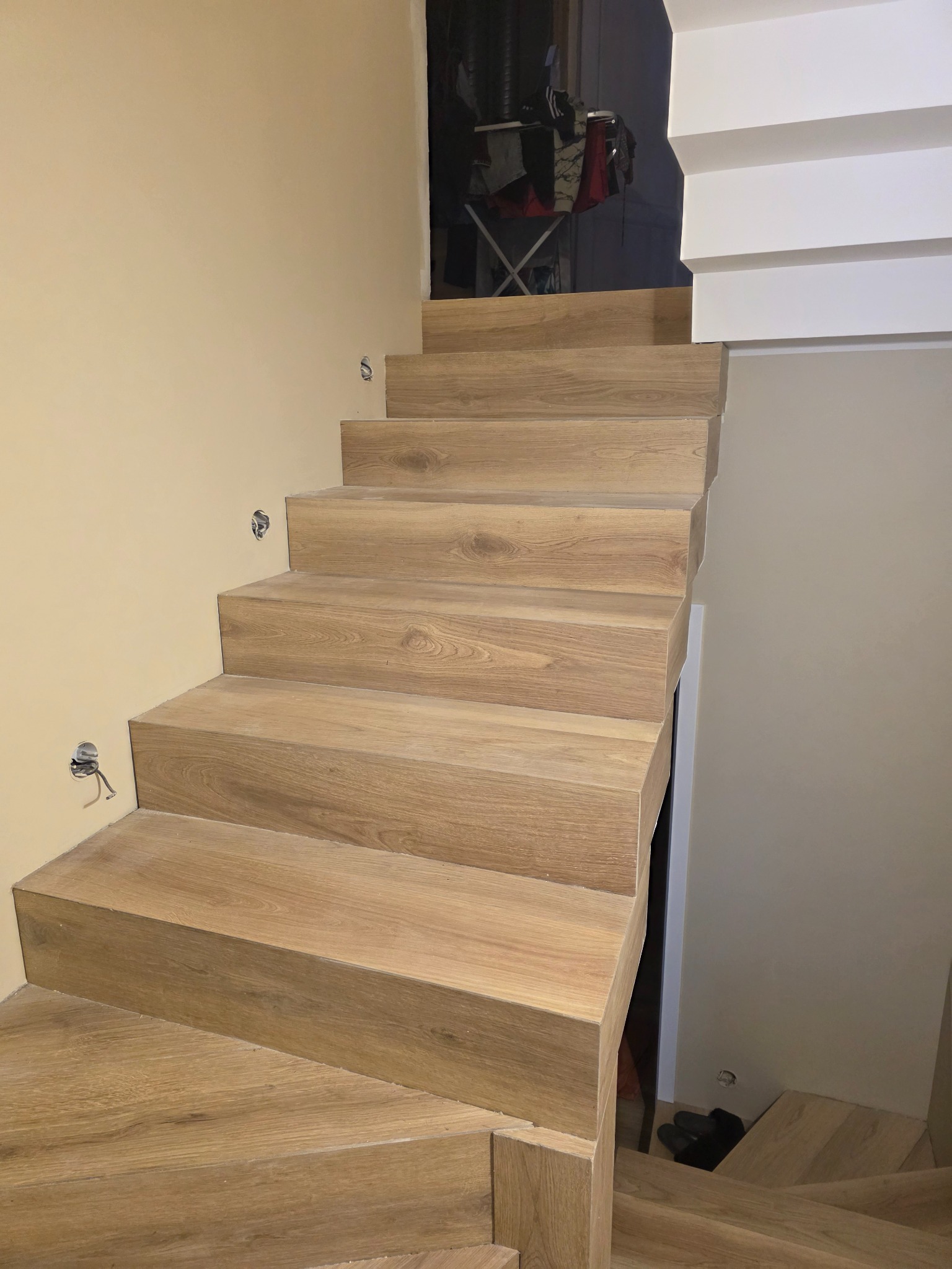 Wykończone schody z drewnopodobnych paneli, widok z dołu. Na ścianie widoczne puszki elektryczne. Ukończony projekt schodów w domu.