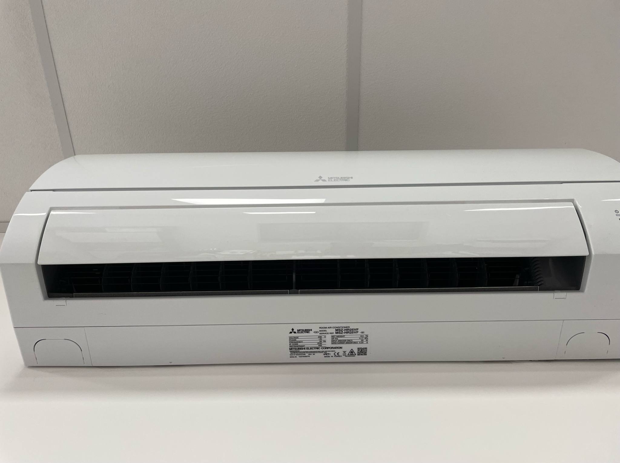 Biała jednostka wewnętrzna klimatyzacji Mitsubishi Electric, model MSZ-HR25VF, zamontowana przy suficie. Widoczna etykieta z danymi technicznymi.