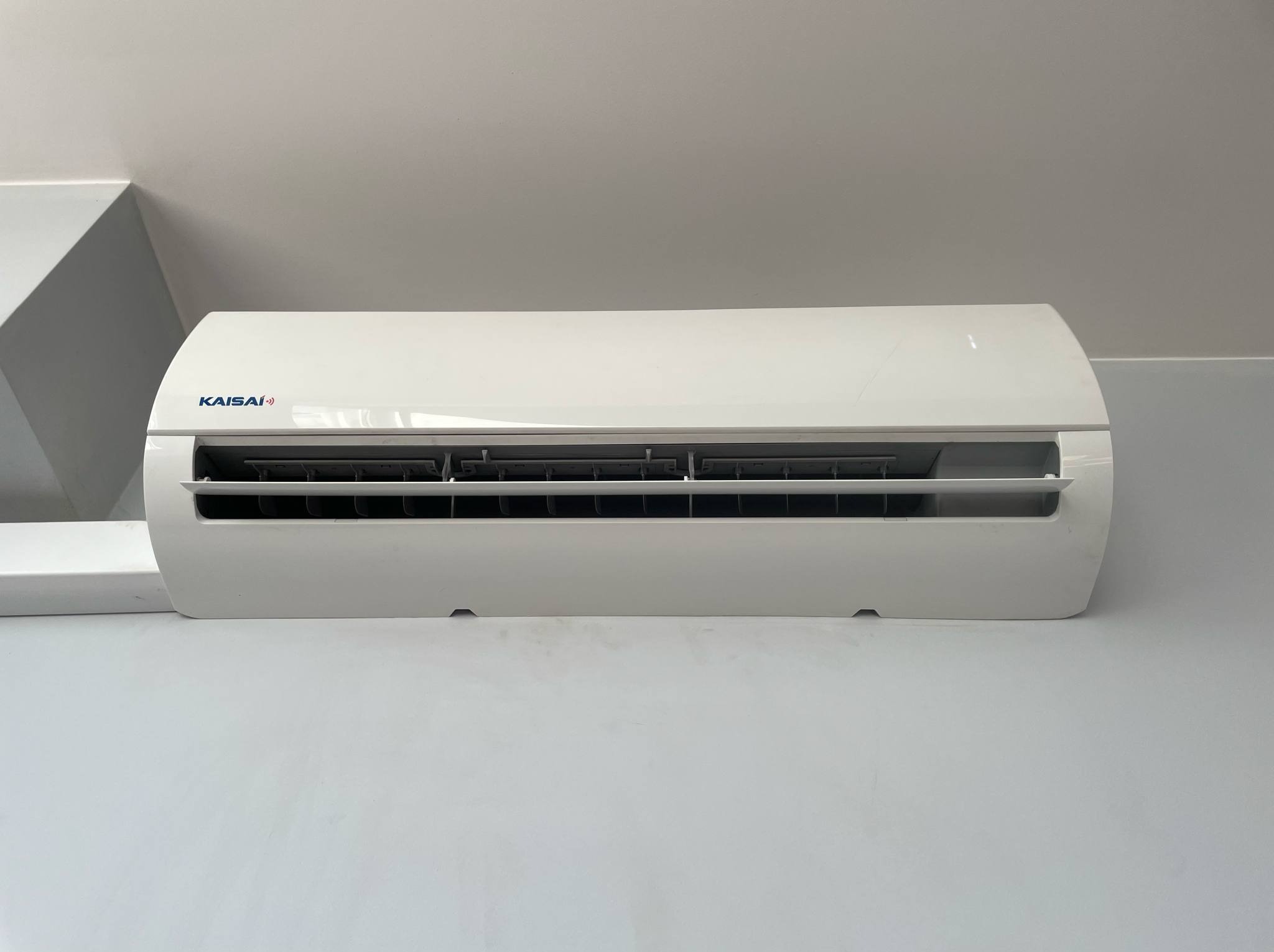 Biała jednostka wewnętrzna klimatyzacji Kaisai, zamontowana na ścianie, widok z dołu, minimalistyczny design, jasne wnętrze.