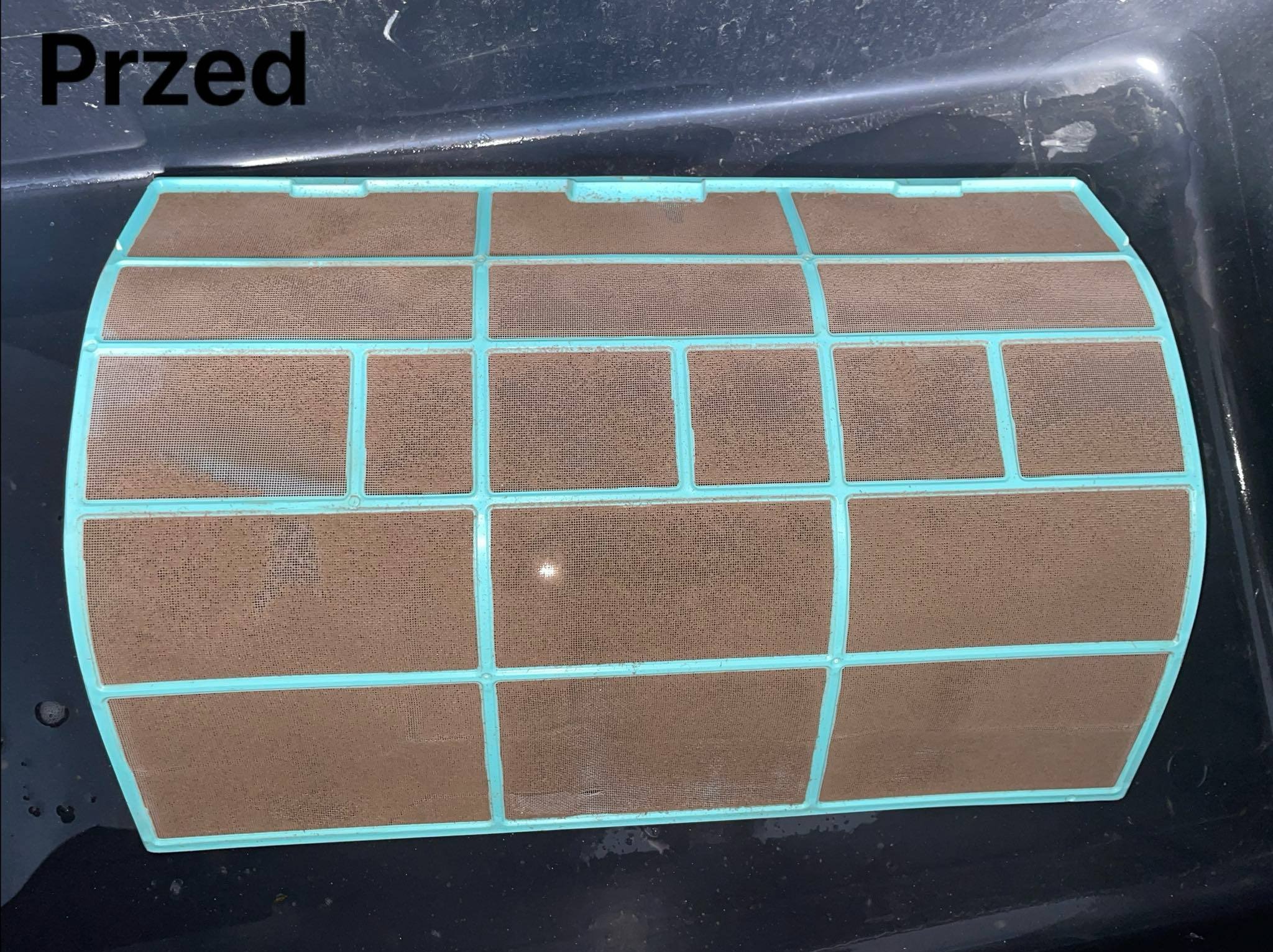 Brudny filtr klimatyzacji w plastikowej ramce, widoczny stan 'przed' czyszczeniem, zanieczyszczenia na siatce filtra.