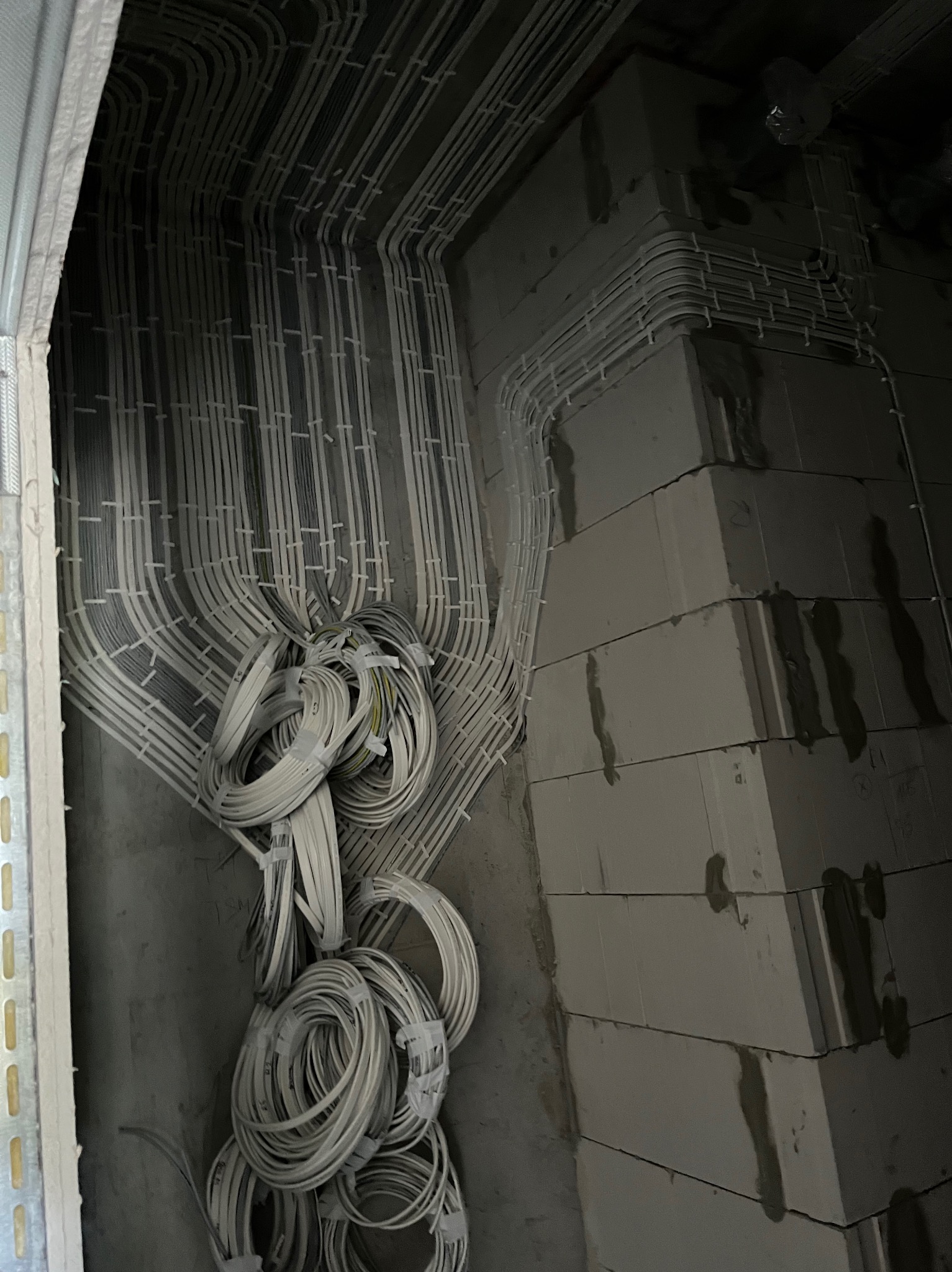 Szczegółowe ułożenie przewodów elektrycznych w peszlach, prowadzone wzdłuż ściany z betonu komórkowego, z widocznymi zwojami kabli i elementami montażowymi.