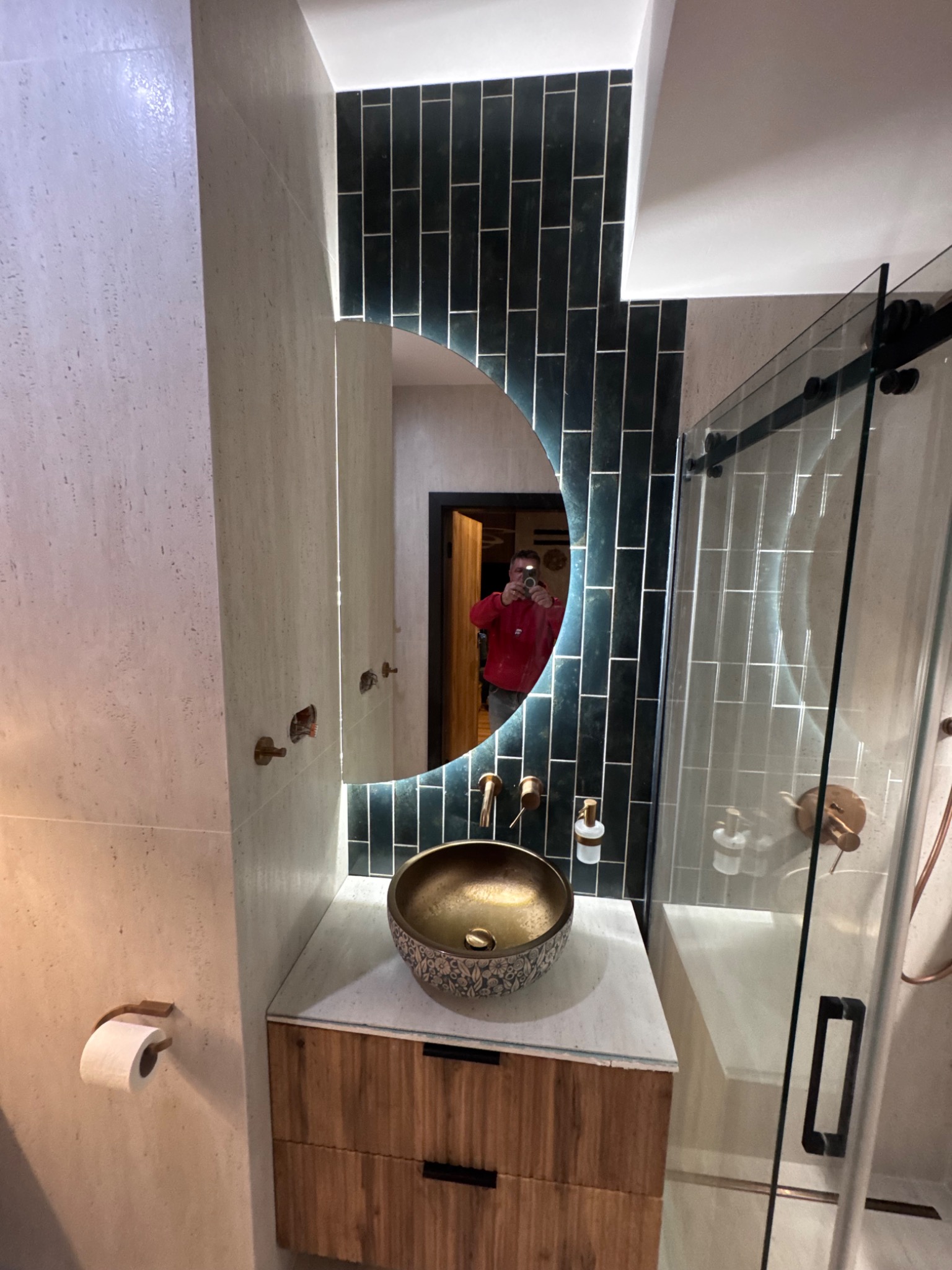 Nowoczesna łazienka z umywalką w stylu boho, podświetlanym lustrem i kabiną prysznicową ze szklanymi drzwiami. Ciemne, pionowe płytki dodają elegancji.