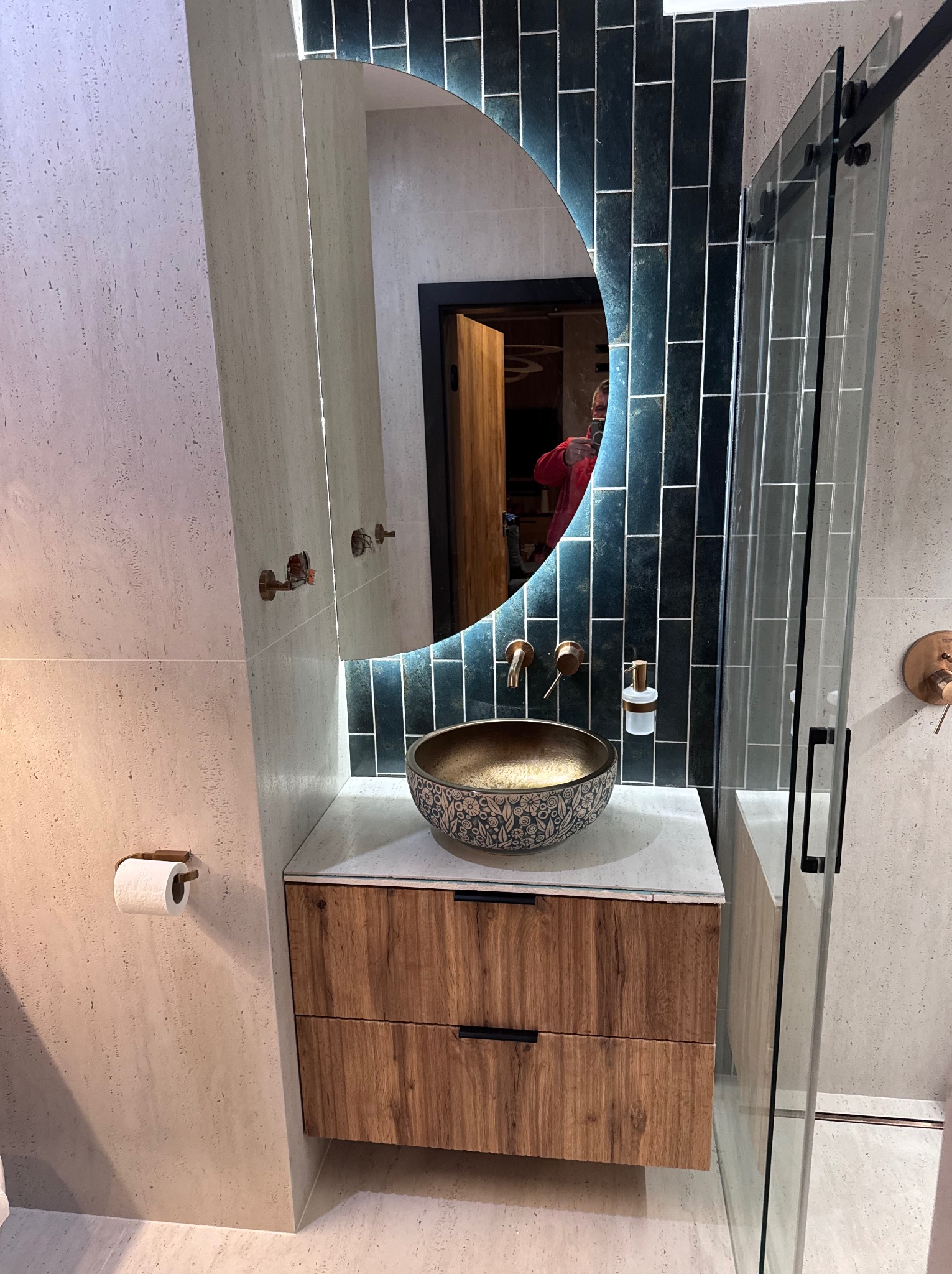 Nowoczesna łazienka po remoncie: umywalka nablatowa z wzorem, drewniana szafka, podświetlane lustro w kształcie półksiężyca, kabina prysznicowa ze szklanymi drzwiami.