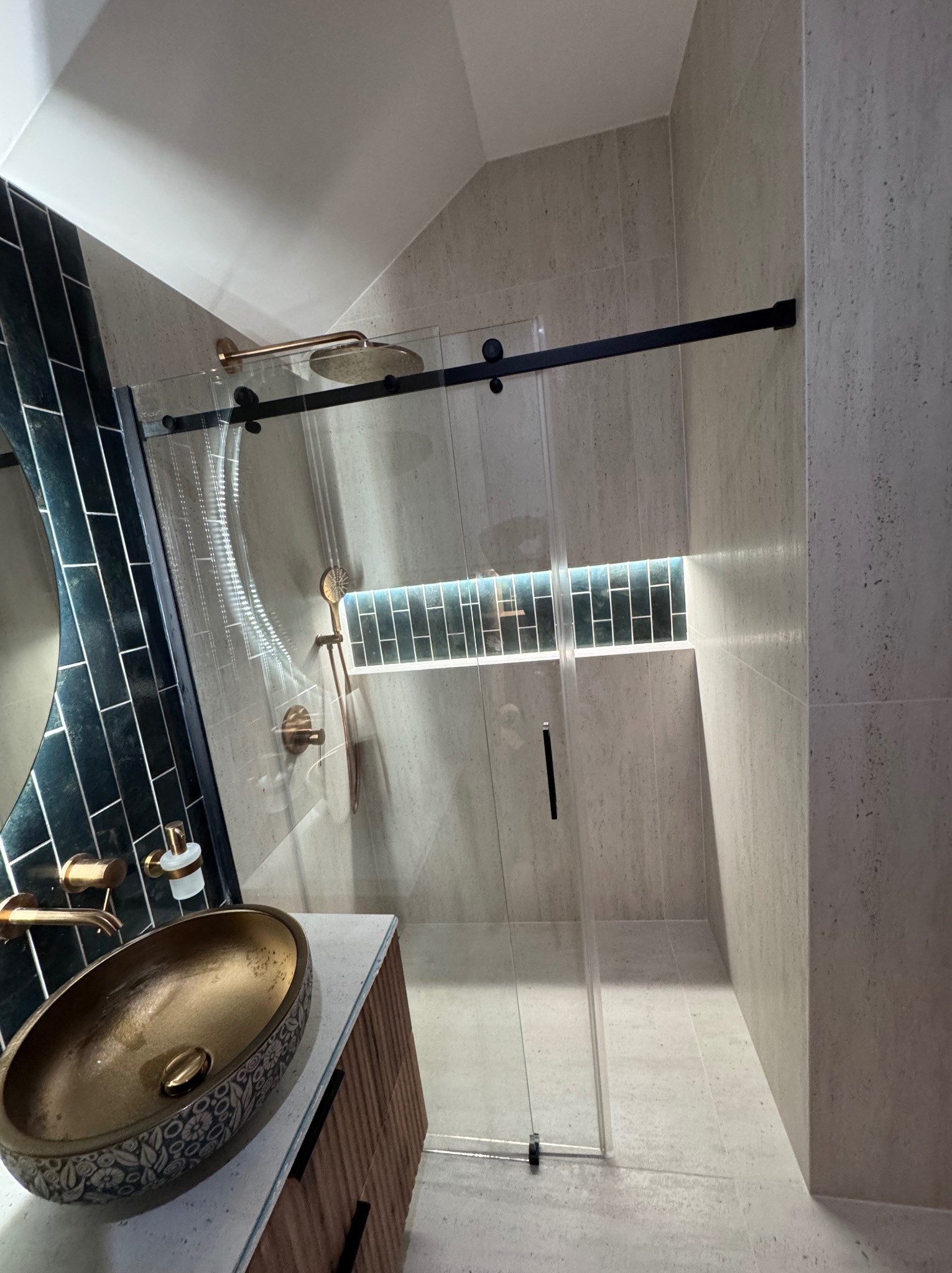 Nowoczesna łazienka z kabiną prysznicową typu walk-in, umywalką w kolorze złota i czarnymi płytkami. Minimalistyczny design z akcentami w odcieniach złota.