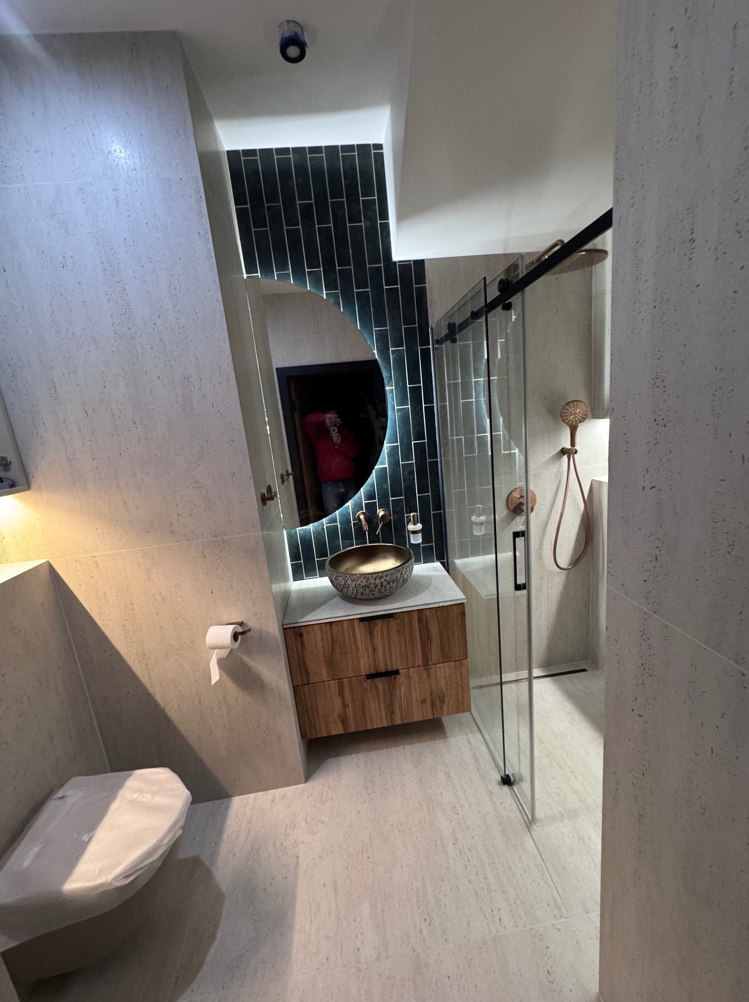 Nowoczesna łazienka w Warszawie: umywalka nablatowa z drewnianą szafką, podświetlane lustro, kabina prysznicowa ze złotą armaturą i toaleta z osłoną.