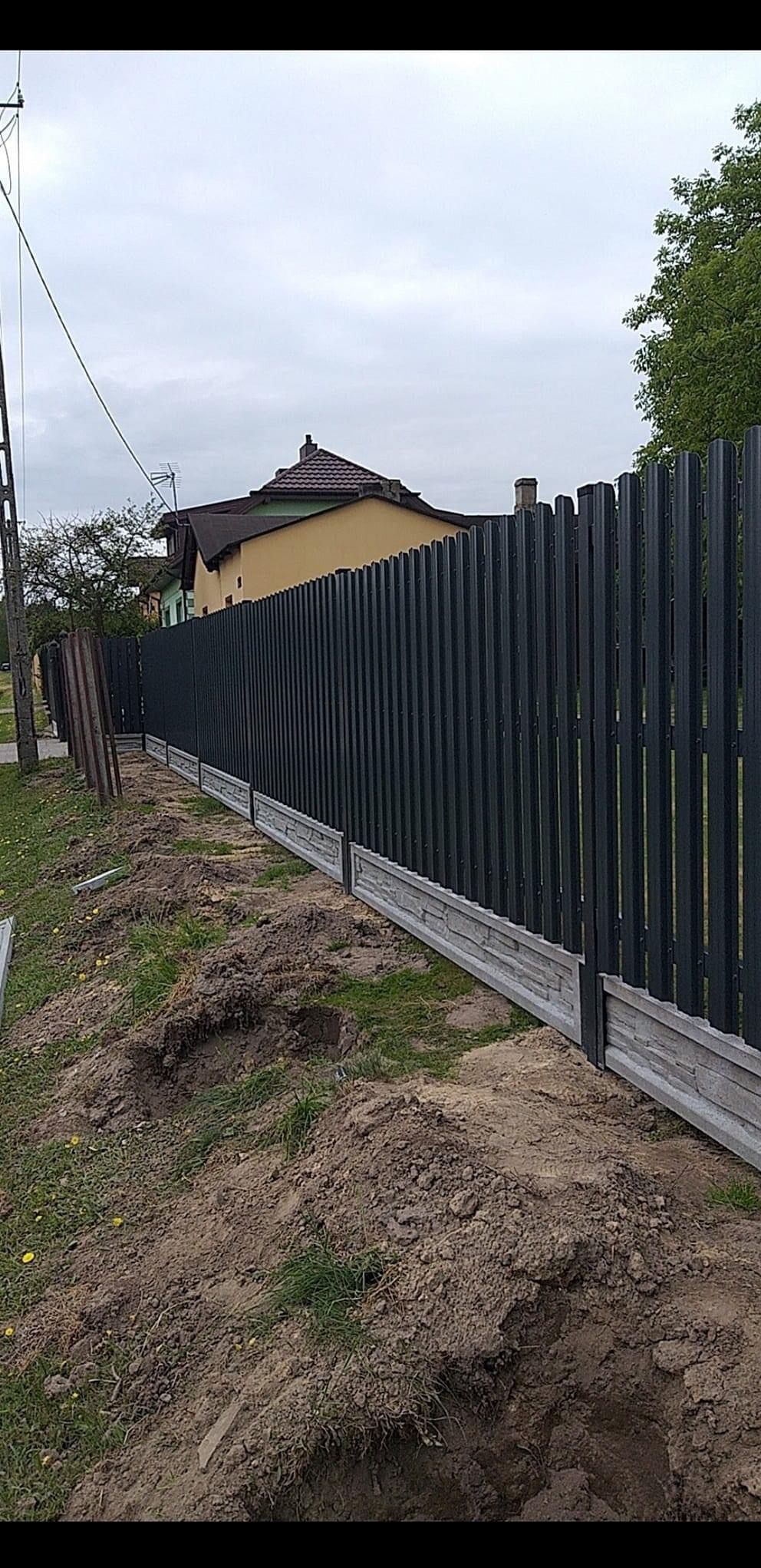 Nowoczesne ogrodzenie metalowe z podmurówką w Różycy. Pionowe panele w kolorze antracytowym, betonowa podmurówka imitująca kamień. Świeżo zamontowane, widoczne ślady prac ziemnych.