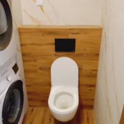 Nowoczesna toaleta podwieszana z drewnianą obudową i marmurowymi płytkami w łazience z pralką. Minimalistyczny design, ciepłe oświetlenie.