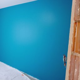 Dominik Hryciuk - Ściana pomalowana na turkusowo, widok z dołu, z fragmentem zakrytej folią podłogi i surowym murem. Widoczna puszka elektryczna. Świeżo po malowaniu.