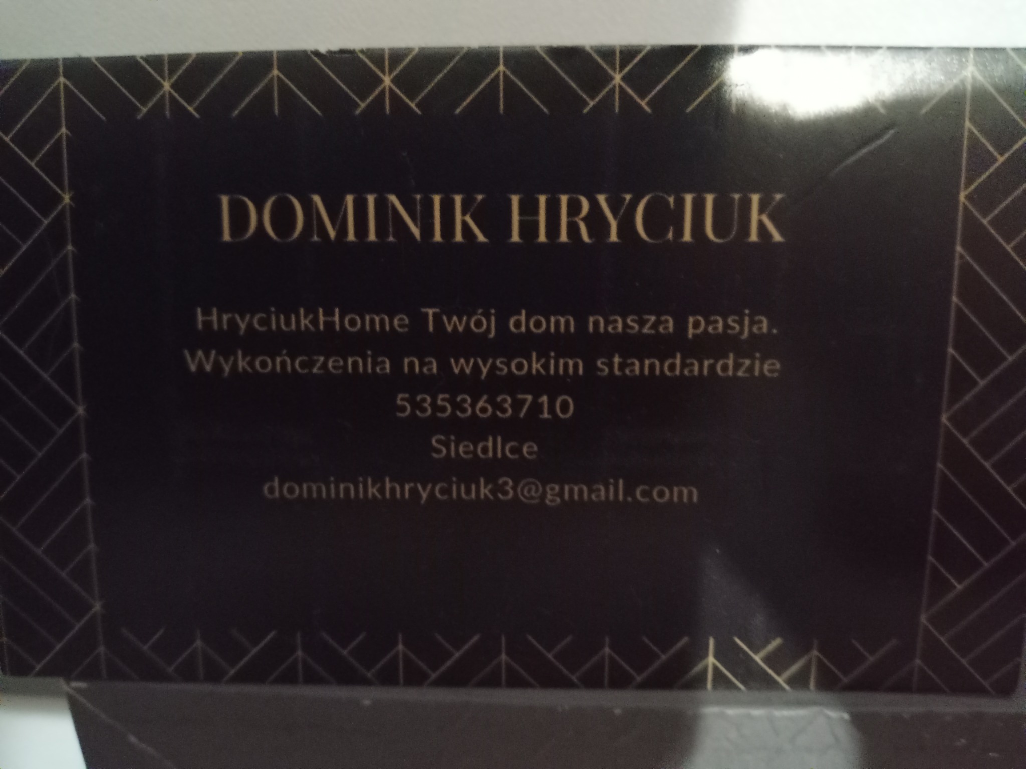 Elegancka wizytówka z imieniem Dominik Hryciuk, hasłem 'Twój dom nasza pasja' i danymi kontaktowymi na ciemnym tle z geometrycznym wzorem w kolorze złota.