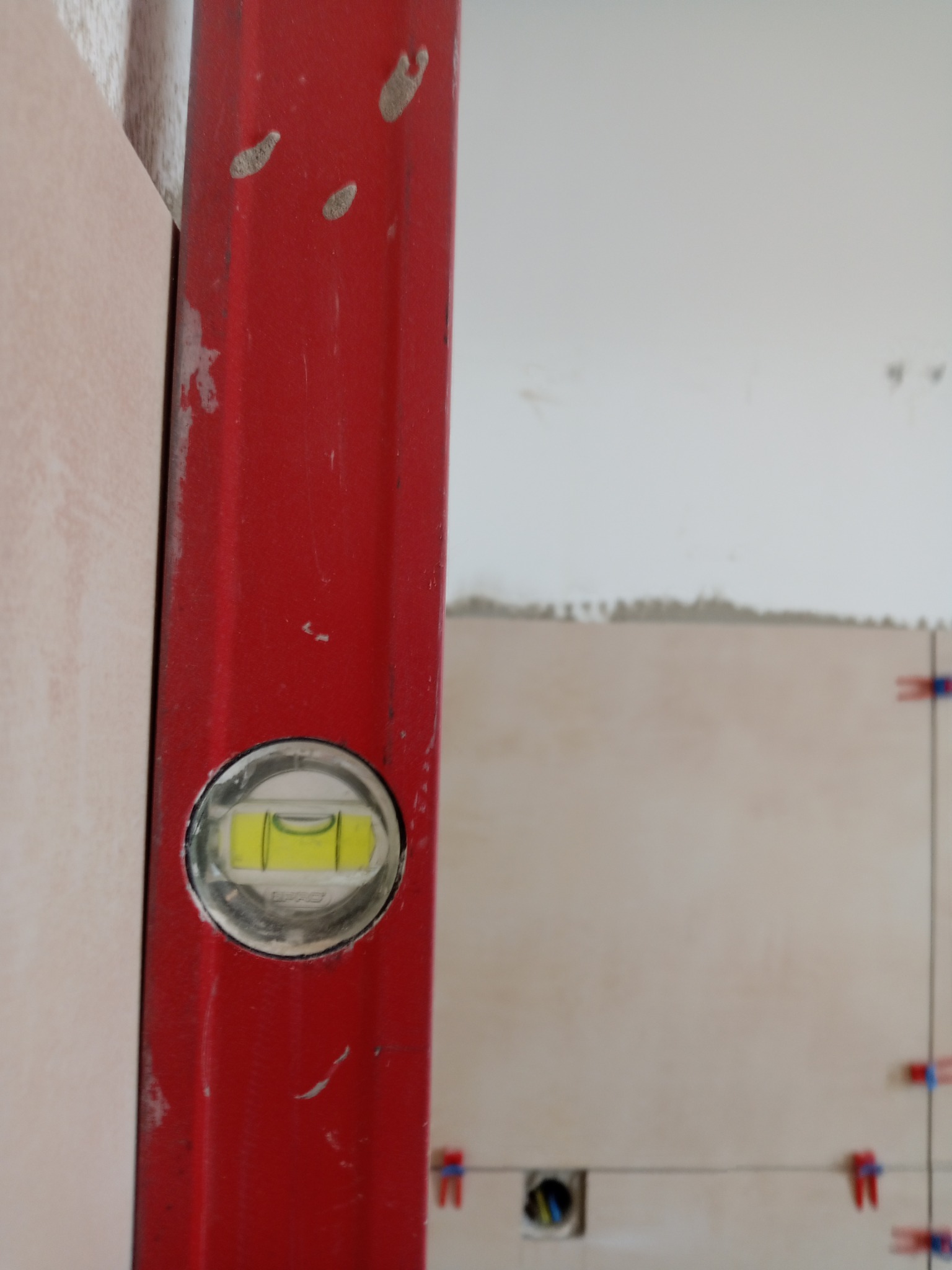 Czerwona poziomica przy beżowych płytkach w trakcie układania. Widoczne krzyżyki dystansowe. Prace glazurnicze w Siedlcach.