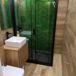 DOM-ART - Nowoczesna łazienka z kabiną prysznicową typu walk-in, wykończona płytkami imitującymi drewno i ścianą z mchu. Umywalka nablatowa na drewnianej szafce.