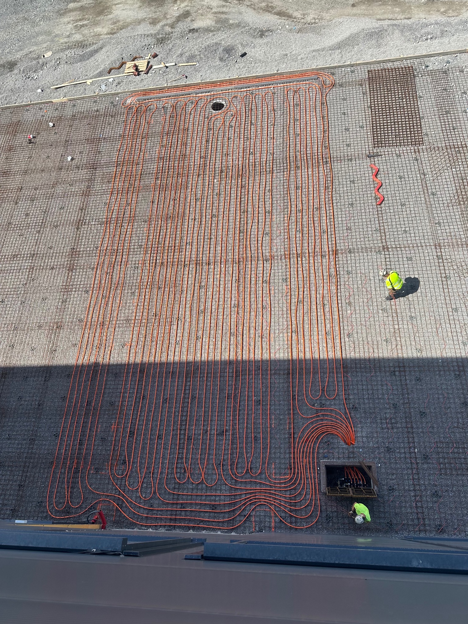 Montaż ogrzewania podłogowego w Malborku. Widok z góry na rozłożone rury grzewcze na siatce zbrojeniowej. Pracownik w kasku przy studzience.