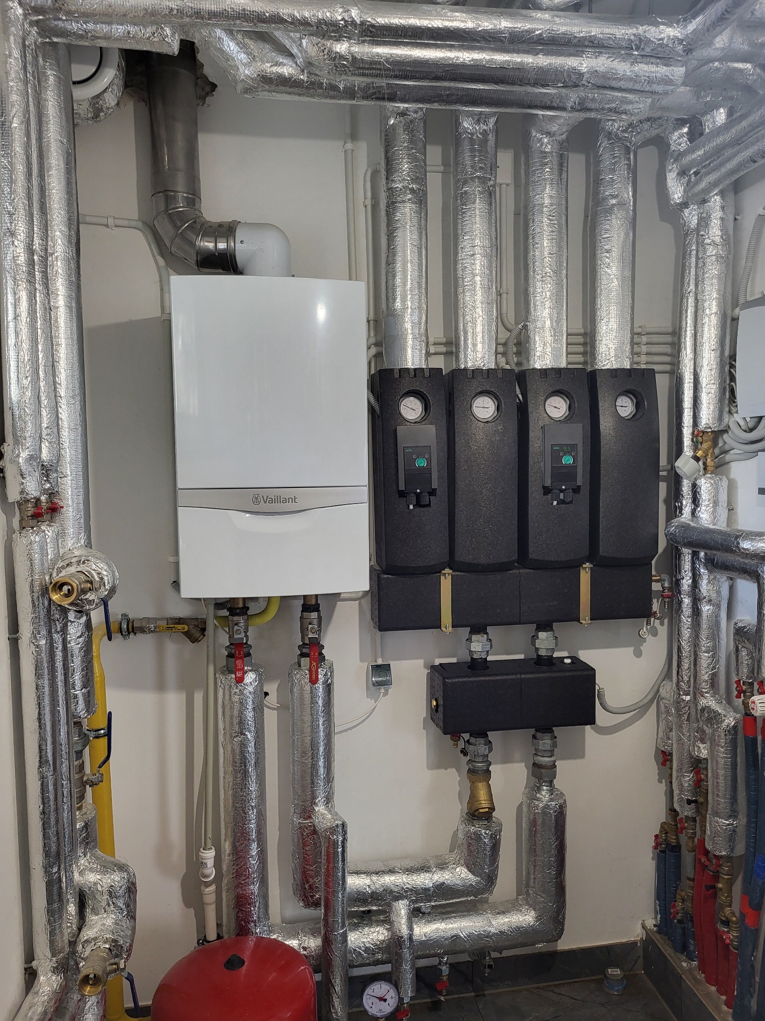 Biały piec gazowy Vaillant i czarne moduły obok, rury w izolacji termicznej, instalacja CO w Gdańsku. Manometry i zawory widoczne.