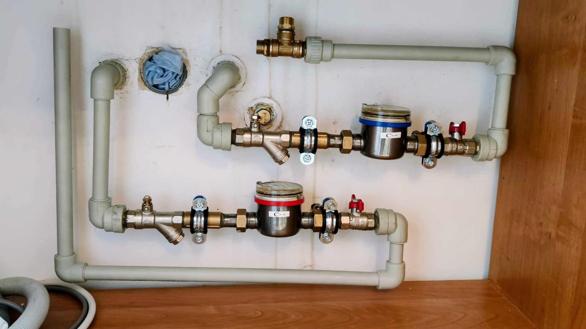 Dwa liczniki wody z zaworami i rurami, zamontowane na ścianie w Warszawie. Widoczne elementy instalacji hydraulicznej oraz fragment szafki.