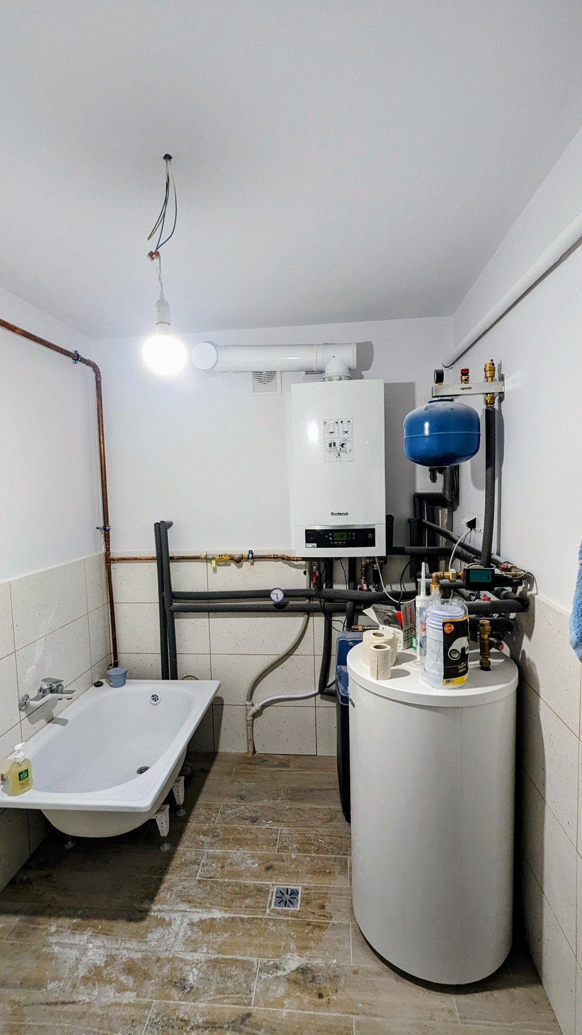 Biały piec gazowy Buderus z niebieskim zbiornikiem wyrównawczym i białym zasobnikiem ciepłej wody w łazience z wanną i wykończoną instalacją hydrauliczną.