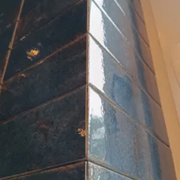 Położone, błyszczące, ciemnoniebieskie płytki w kształcie cegiełek na rogu ściany, widoczne z bliska. Usługa glazurnicza w Lubinie.