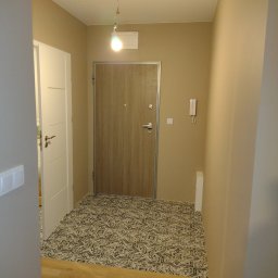 VOKMIS BUD SERHII SIMKOV - Korytarz po remoncie: beżowe ściany, drewnopodobna podłoga i wzorzysta posadzka przy drzwiach wejściowych. Widoczny biały włącznik światła i domofon.