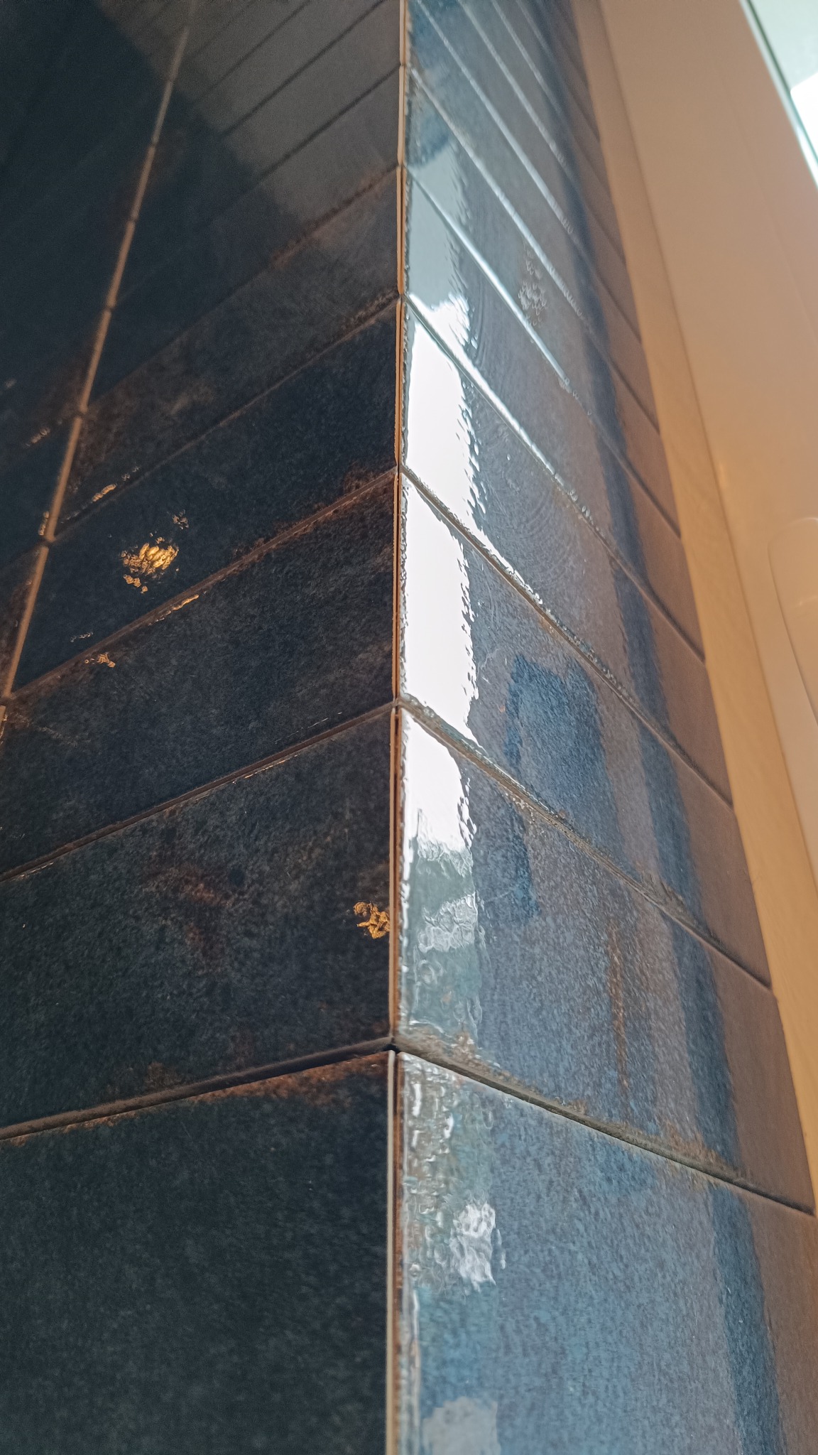 Położone, błyszczące, ciemnoniebieskie płytki w kształcie cegiełek na rogu ściany, widoczne z bliska. Usługa glazurnicza w Lubinie.