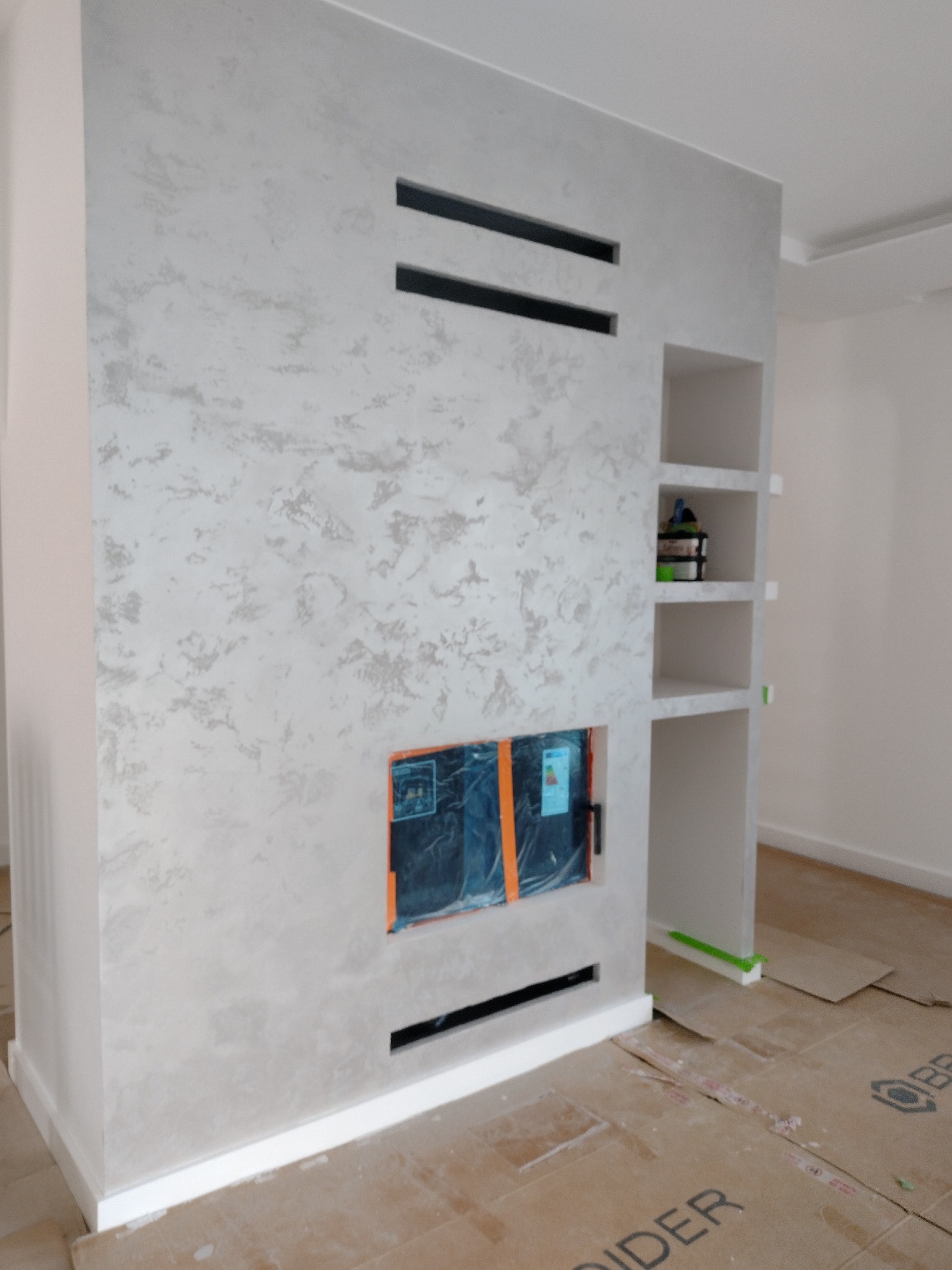 Ściana dekoracyjna z efektem stiuku w Lubinie, z wnękami i otworem na kominek zabezpieczonym folią. Wykończenie wnętrza w nowoczesnym stylu.