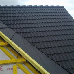 Usługi budowlane - Częściowy widok dachu z czarną dachówką na drewnianej więźbie, z widoczną membraną dachową. Ujęcie z bliska, z perspektywy od dołu.