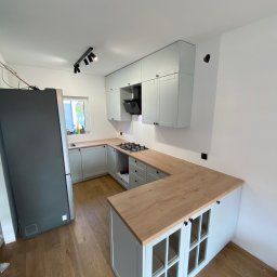 Stepan Malitskyi Standem Bud - Jasna kuchnia po remoncie: białe ściany, drewniana podłoga, szare meble z drewnianym blatem. Nowoczesne oświetlenie punktowe. Widoczna płyta gazowa i szary lodówka.