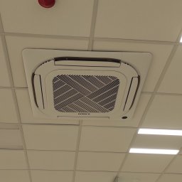 Nsinstal klimatyzacja wentylacja rekuperacja - Biała, kasetonowa klimatyzacja sufitowa marki Kaisai, zamontowana w biurze z oświetleniem rastrowym. Widok z dołu, centralne ujęcie.