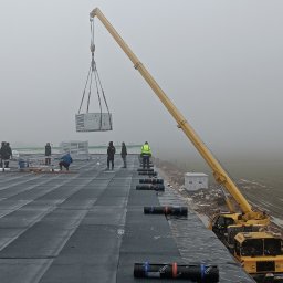 Nsinstal klimatyzacja wentylacja rekuperacja - Montaż klimatyzacji na dachu budynku komercyjnego. Żuraw podnosi jednostkę klimatyzacyjną, a grupa monterów w odblaskowych kamizelkach nadzoruje proces w mglisty dzień.